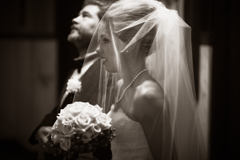 A bride with her veil on standing by her father waiting to walk down the aisle.